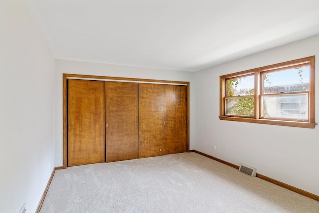 unfurnished bedroom featuring a closet, light colored carpet, visible vents, and baseboards