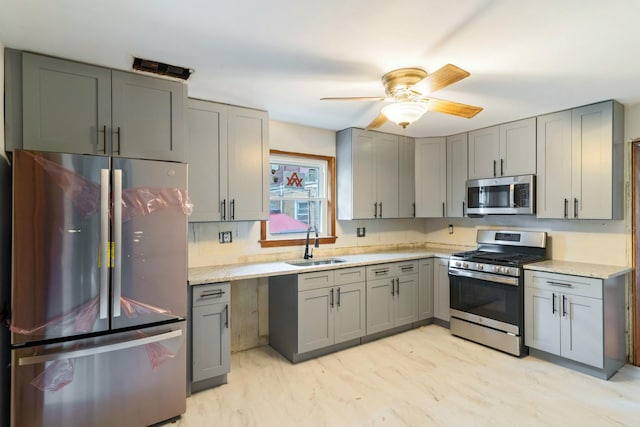 kitchen with appliances with stainless steel finishes, a sink, gray cabinetry, and a ceiling fan