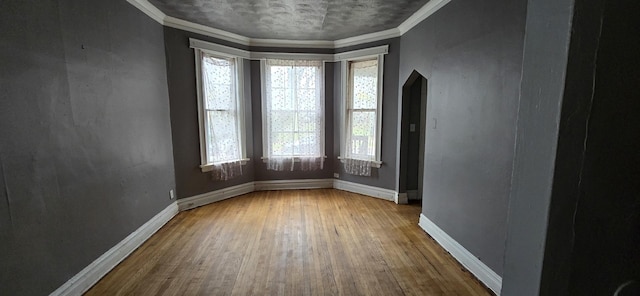 unfurnished room featuring baseboards, wood-type flooring, and crown molding