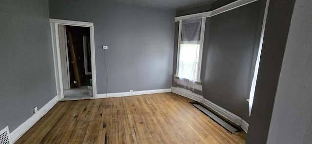 unfurnished room with a baseboard heating unit, baseboards, and hardwood / wood-style flooring