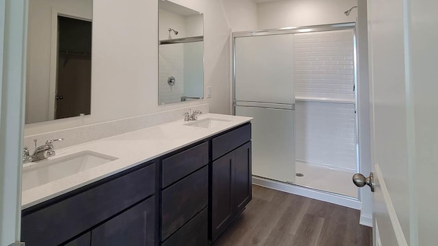 full bath with a stall shower, double vanity, a sink, and wood finished floors