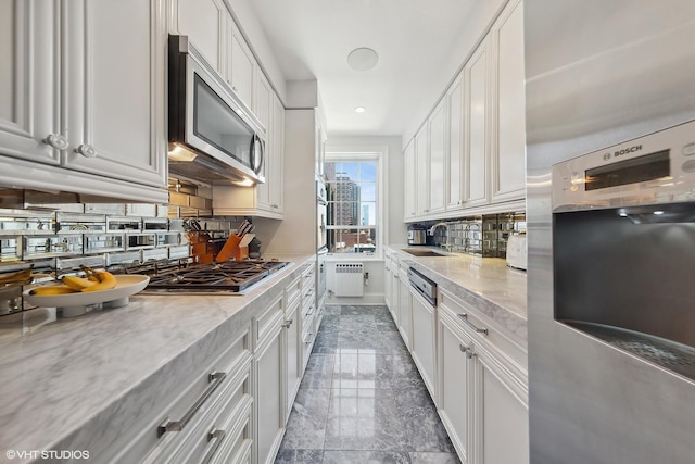 kitchen with radiator heating unit, a sink, marble finish floor, stainless steel appliances, and backsplash