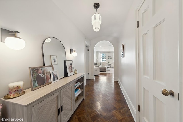 hall featuring arched walkways and baseboards