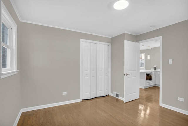 unfurnished bedroom featuring baseboards, visible vents, wood finished floors, and ornamental molding