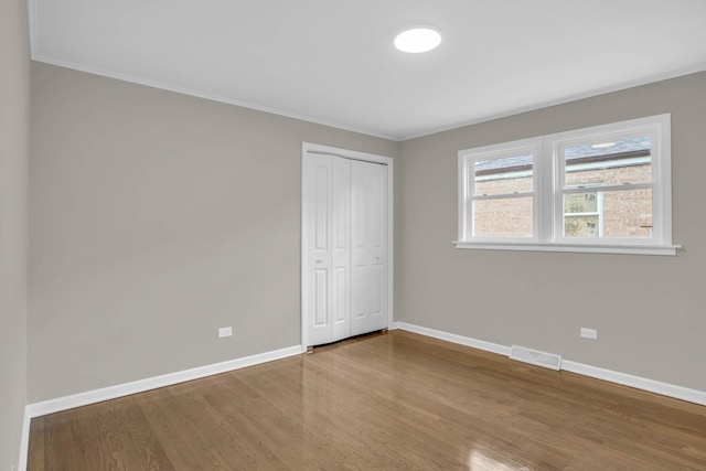 unfurnished bedroom with a closet, visible vents, baseboards, and wood finished floors