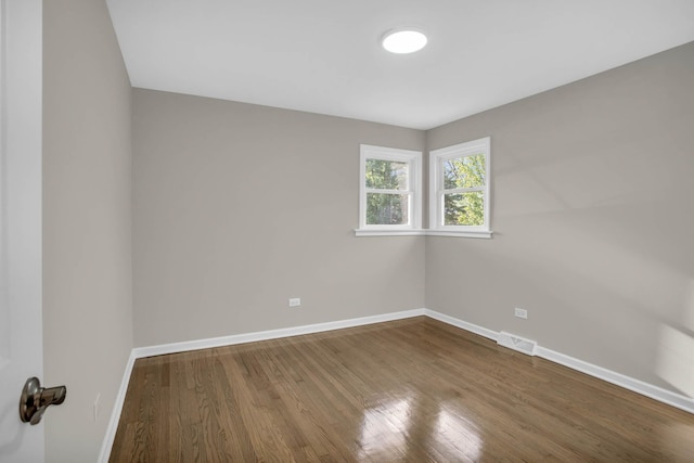 empty room with wood finished floors, visible vents, and baseboards