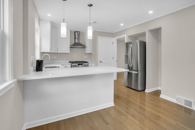 kitchen with visible vents, wall chimney exhaust hood, a peninsula, stainless steel appliances, and light countertops