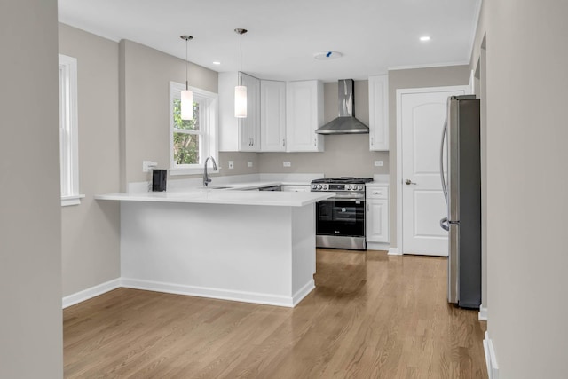 kitchen featuring a peninsula, a sink, white cabinetry, appliances with stainless steel finishes, and wall chimney exhaust hood