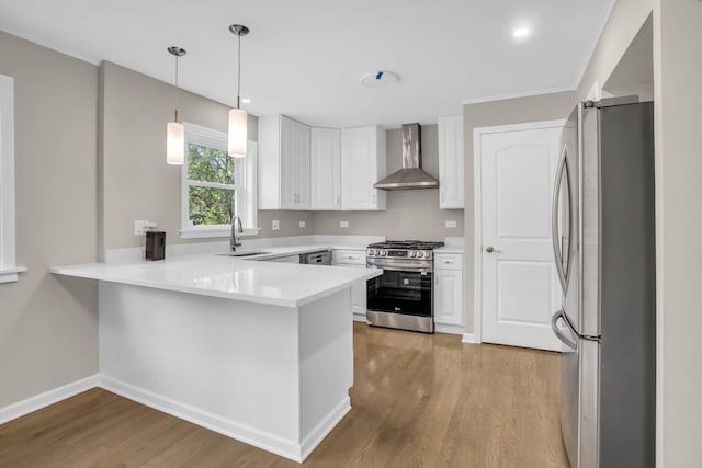 kitchen featuring appliances with stainless steel finishes, light wood-style floors, a sink, wall chimney range hood, and a peninsula