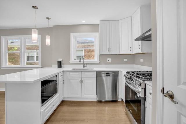 kitchen featuring a peninsula, a sink, white cabinetry, appliances with stainless steel finishes, and wall chimney range hood