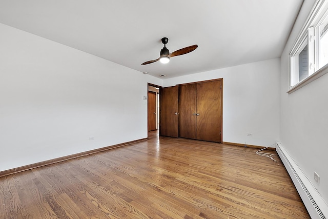 unfurnished bedroom featuring a baseboard heating unit, light wood-type flooring, a closet, and baseboards