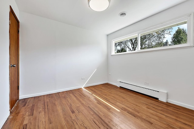 unfurnished room with a baseboard radiator, visible vents, baseboards, and wood finished floors