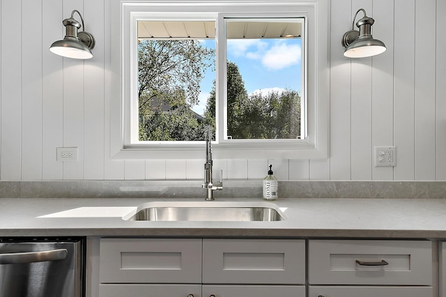 kitchen featuring light countertops, stainless steel dishwasher, a sink, and decorative light fixtures