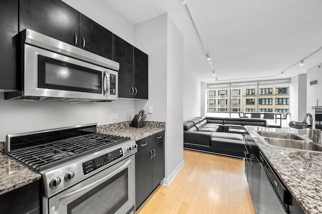 kitchen featuring light wood finished floors, appliances with stainless steel finishes, a sink, and dark cabinets