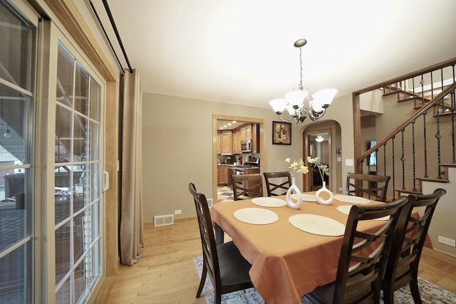 dining room with arched walkways, visible vents, light wood-style flooring, an inviting chandelier, and stairs