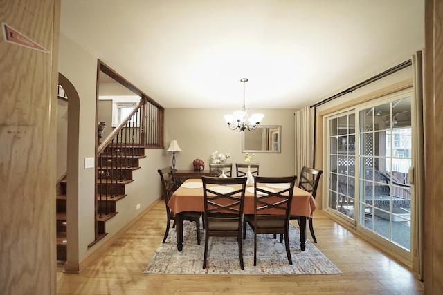 dining area with light wood-style floors, a notable chandelier, baseboards, and stairs