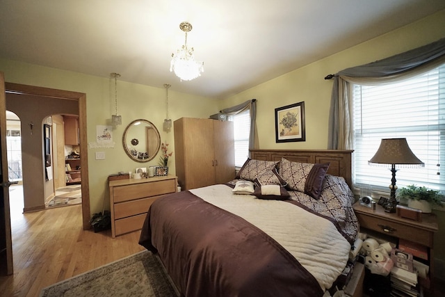 bedroom with arched walkways, light wood-type flooring, and an inviting chandelier