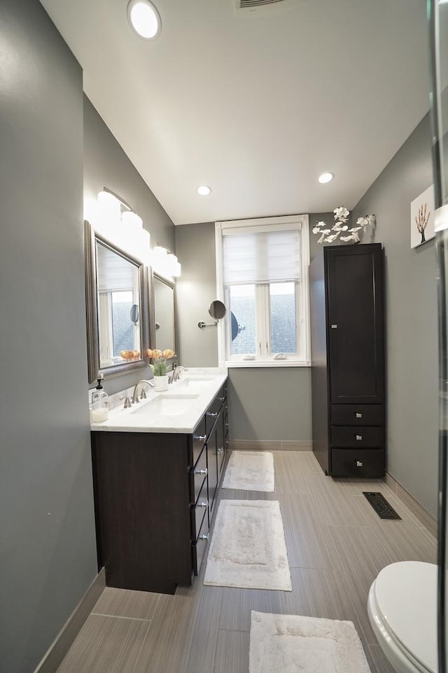 bathroom featuring toilet, a sink, visible vents, baseboards, and double vanity