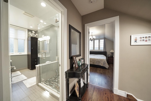 ensuite bathroom featuring lofted ceiling, a stall shower, wood finished floors, and baseboards