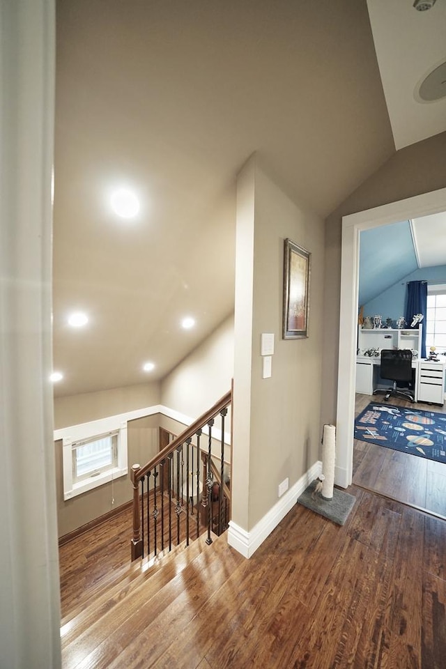 hallway featuring vaulted ceiling, an upstairs landing, hardwood / wood-style flooring, and baseboards