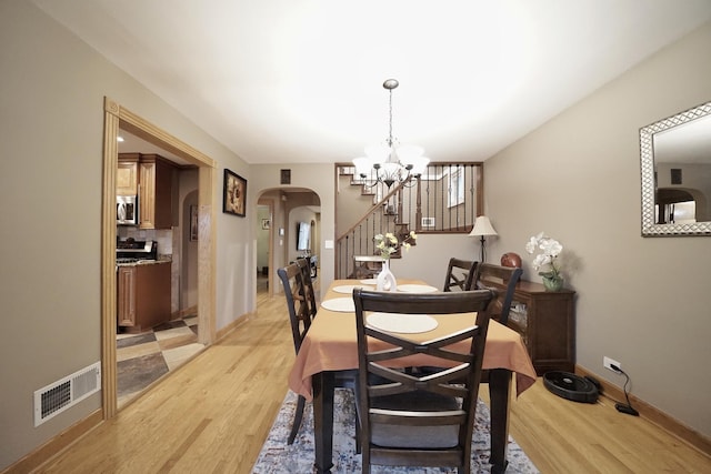 dining space featuring light wood finished floors, visible vents, arched walkways, and a chandelier