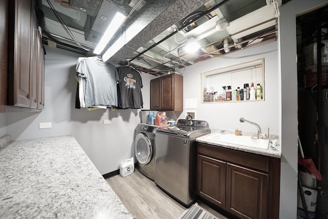 laundry area with cabinet space, light wood-style flooring, washing machine and dryer, a sink, and baseboards