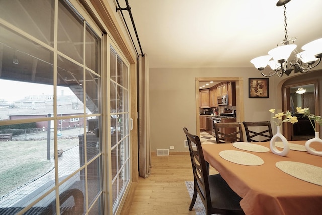 dining space with baseboards, light wood finished floors, visible vents, and a notable chandelier