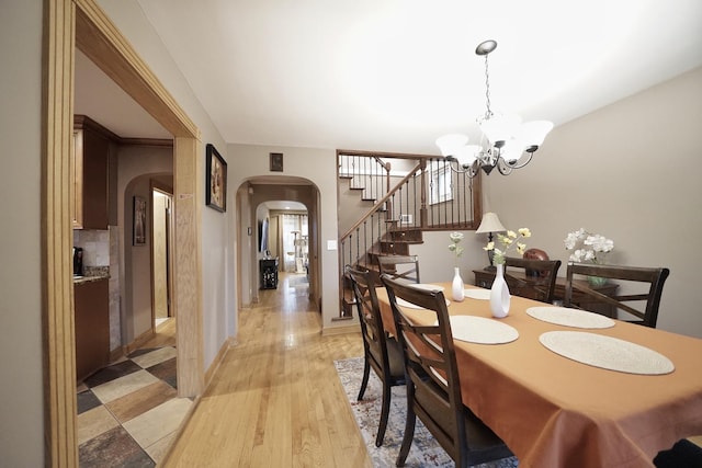 dining room featuring baseboards, arched walkways, stairs, light wood-type flooring, and a notable chandelier