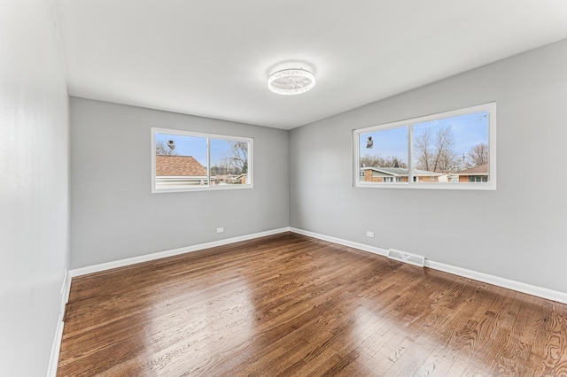 unfurnished room with wood finished floors, baseboards, visible vents, and a wealth of natural light