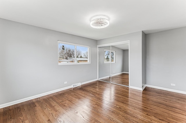 unfurnished bedroom with a closet, visible vents, baseboards, and wood finished floors