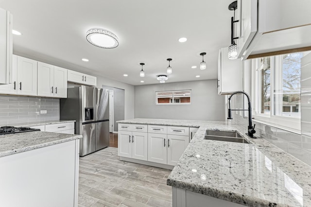 kitchen with tasteful backsplash, stainless steel fridge, a peninsula, white cabinetry, and a sink