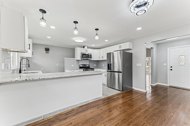 kitchen with a sink, a peninsula, wood finished floors, stainless steel appliances, and decorative backsplash