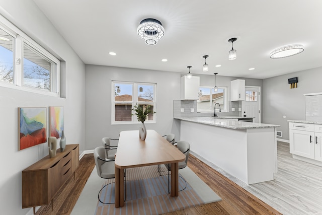 kitchen with a peninsula, white cabinetry, light wood finished floors, decorative backsplash, and light stone counters