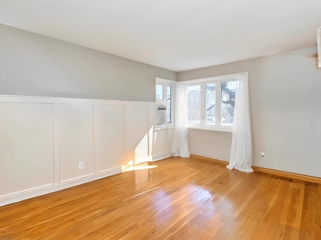 empty room with light wood-type flooring, a wainscoted wall, a decorative wall, and cooling unit