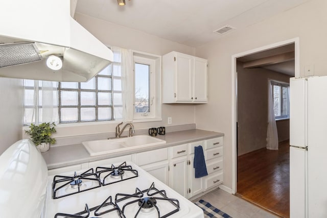 kitchen featuring range with gas cooktop, freestanding refrigerator, white cabinetry, a sink, and exhaust hood