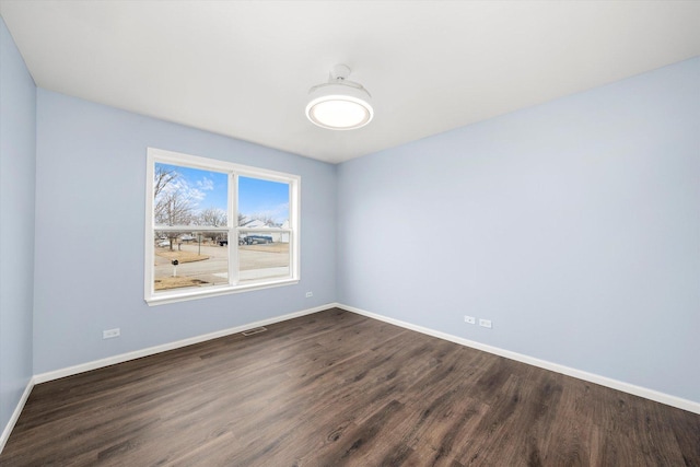 spare room with dark wood-style floors, visible vents, and baseboards