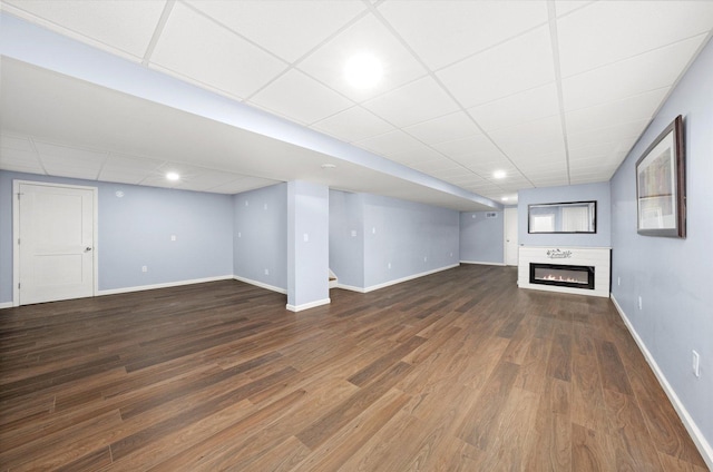 finished basement with a glass covered fireplace, a paneled ceiling, baseboards, and wood finished floors