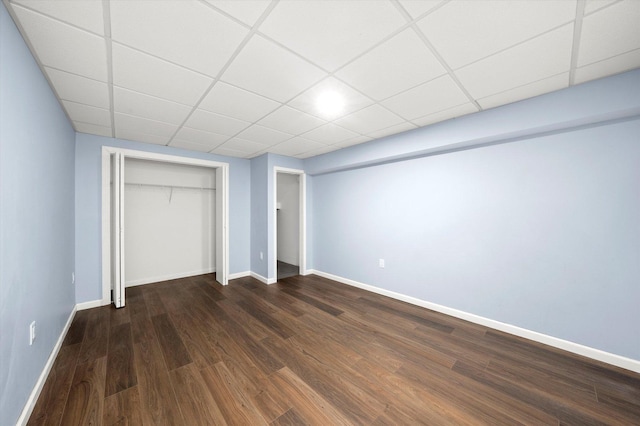 unfurnished bedroom featuring dark wood-style flooring, a drop ceiling, and baseboards