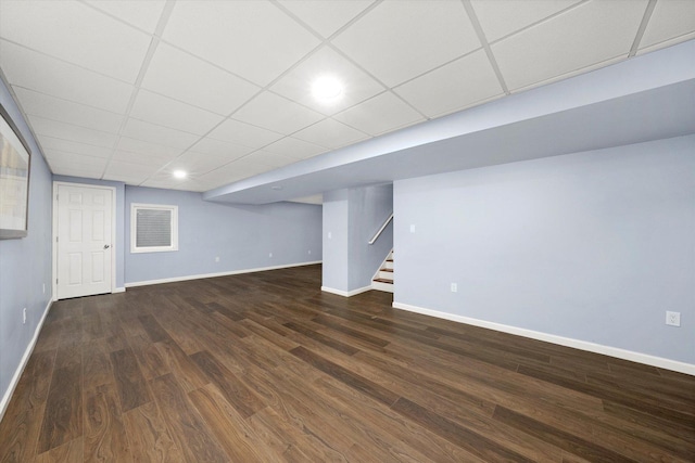 finished basement featuring a paneled ceiling, baseboards, stairway, and dark wood-style flooring