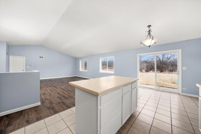 kitchen with light tile patterned floors, lofted ceiling, white cabinetry, hanging light fixtures, and light countertops