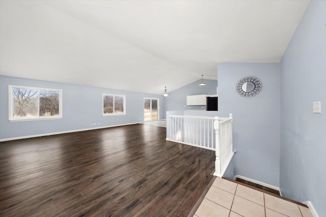 empty room with baseboards, vaulted ceiling, a wealth of natural light, and wood finished floors