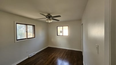 empty room with visible vents, dark wood finished floors, baseboards, and ceiling fan