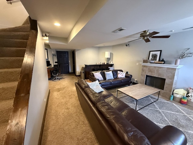 carpeted living room featuring visible vents, ceiling fan, a tiled fireplace, and stairway