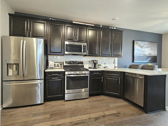 kitchen with appliances with stainless steel finishes, light countertops, a peninsula, and light wood finished floors