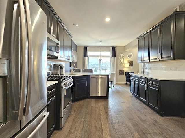 kitchen with tasteful backsplash, light countertops, appliances with stainless steel finishes, wood finished floors, and a peninsula