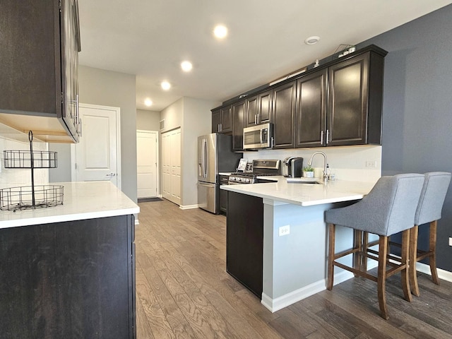 kitchen with stainless steel appliances, a peninsula, wood finished floors, a sink, and a kitchen bar