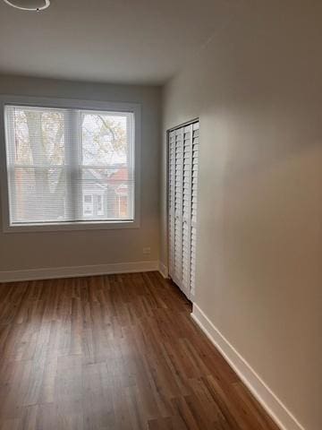 spare room with baseboards and dark wood-type flooring