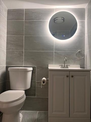 bathroom with toilet, tile walls, and vanity