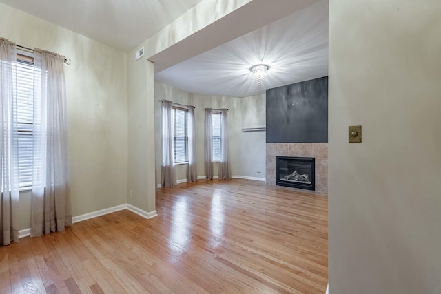 unfurnished living room with light wood-style floors, plenty of natural light, baseboards, and a tile fireplace