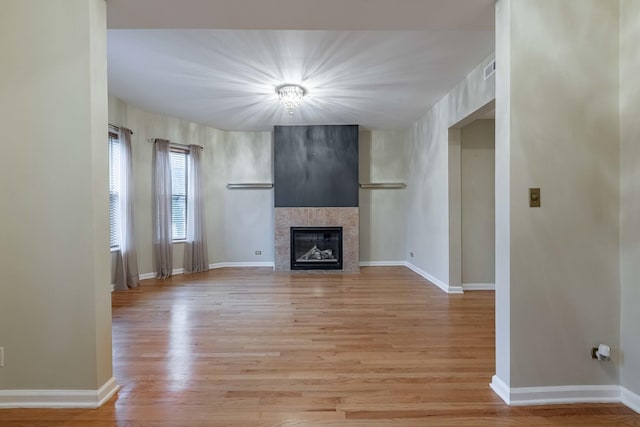 unfurnished living room with light wood finished floors, a tile fireplace, and baseboards